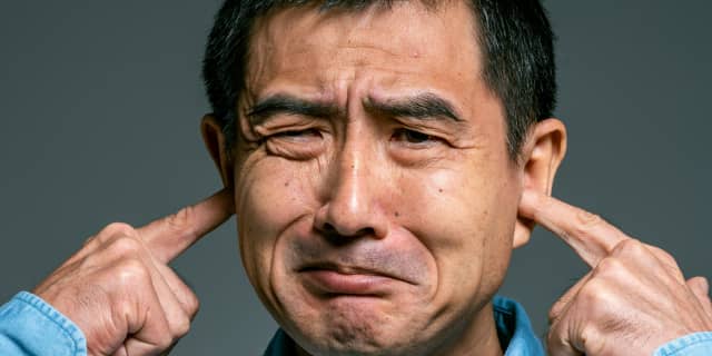 Man plugging ears with unhappy expression