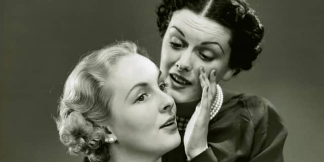 Old monochrome Hollywood picture of a woman whisphering in another woman's ear